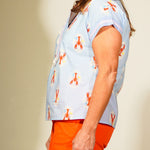Woman wearing a light blue patterned top and orange shorts against a plain background