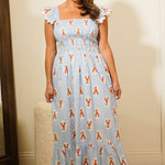 Woman wearing a blue dress with a pattern, standing against a plain wall.