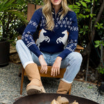 Woman wearing a blue sweater with horse designs sitting by a fire pit outdoors.