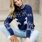 Woman wearing a blue sweater with white patterns sitting on a couch.