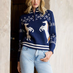 Woman wearing a navy blue sweater with white patterns and light blue jeans, standing indoors.