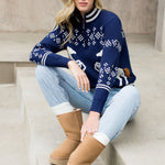 Woman wearing a blue sweater with white patterns, light blue jeans, and tan boots sitting on steps.