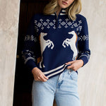 Woman wearing a navy blue sweater with reindeer design and light blue jeans indoors.