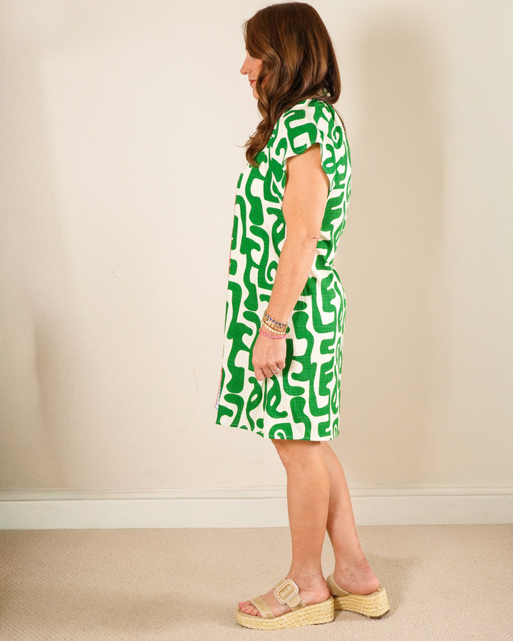 Woman wearing a green and ivory abstract print tunic dress with blue striped neck detail and tan platform sandals.