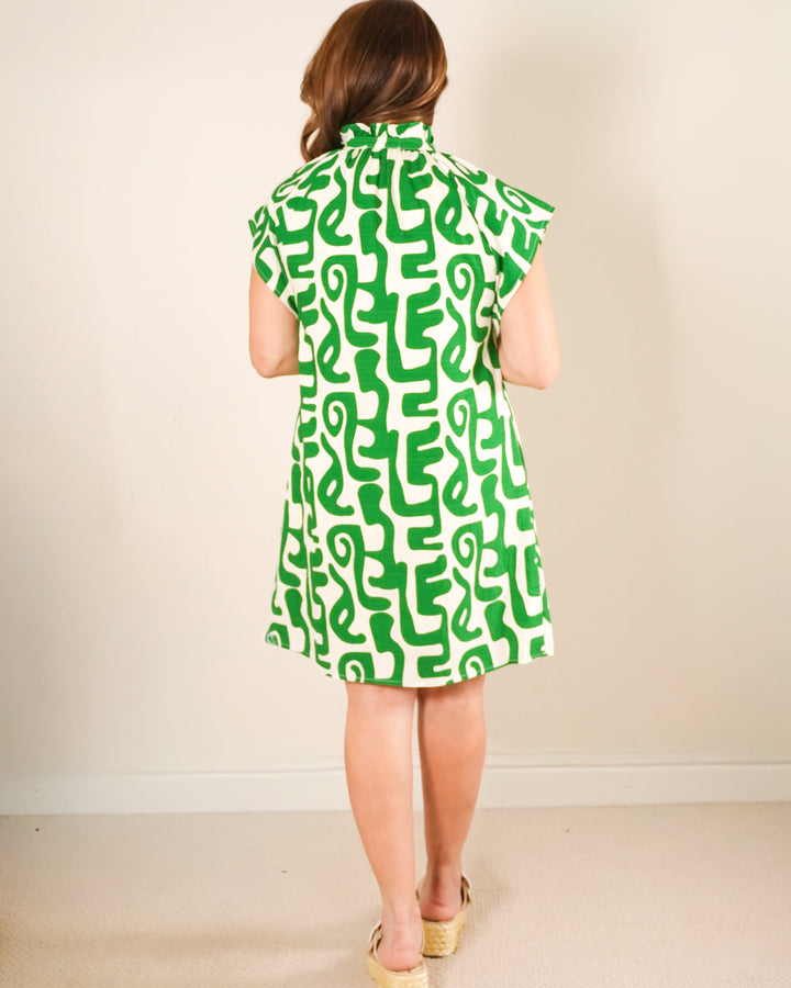 Woman wearing a green and ivory abstract print tunic dress with blue striped neck detail and tan platform sandals.