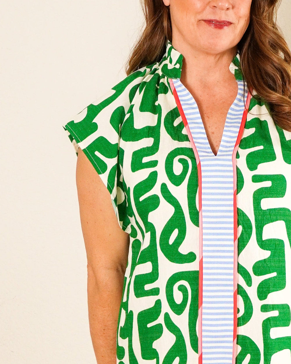 Woman wearing a green and ivory abstract print tunic dress with blue striped neck detail and tan platform sandals.