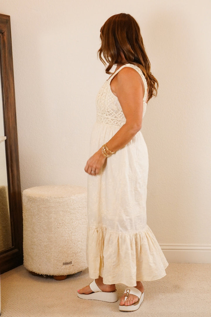 Woman in a white dress standing in a bedroom next to a dresser and mirror.
