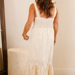 Woman in a white dress standing in a bedroom with a dresser and mirror.