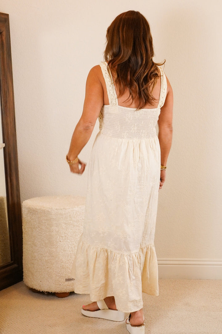 Woman in a white dress standing in a bedroom with a dresser and mirror.