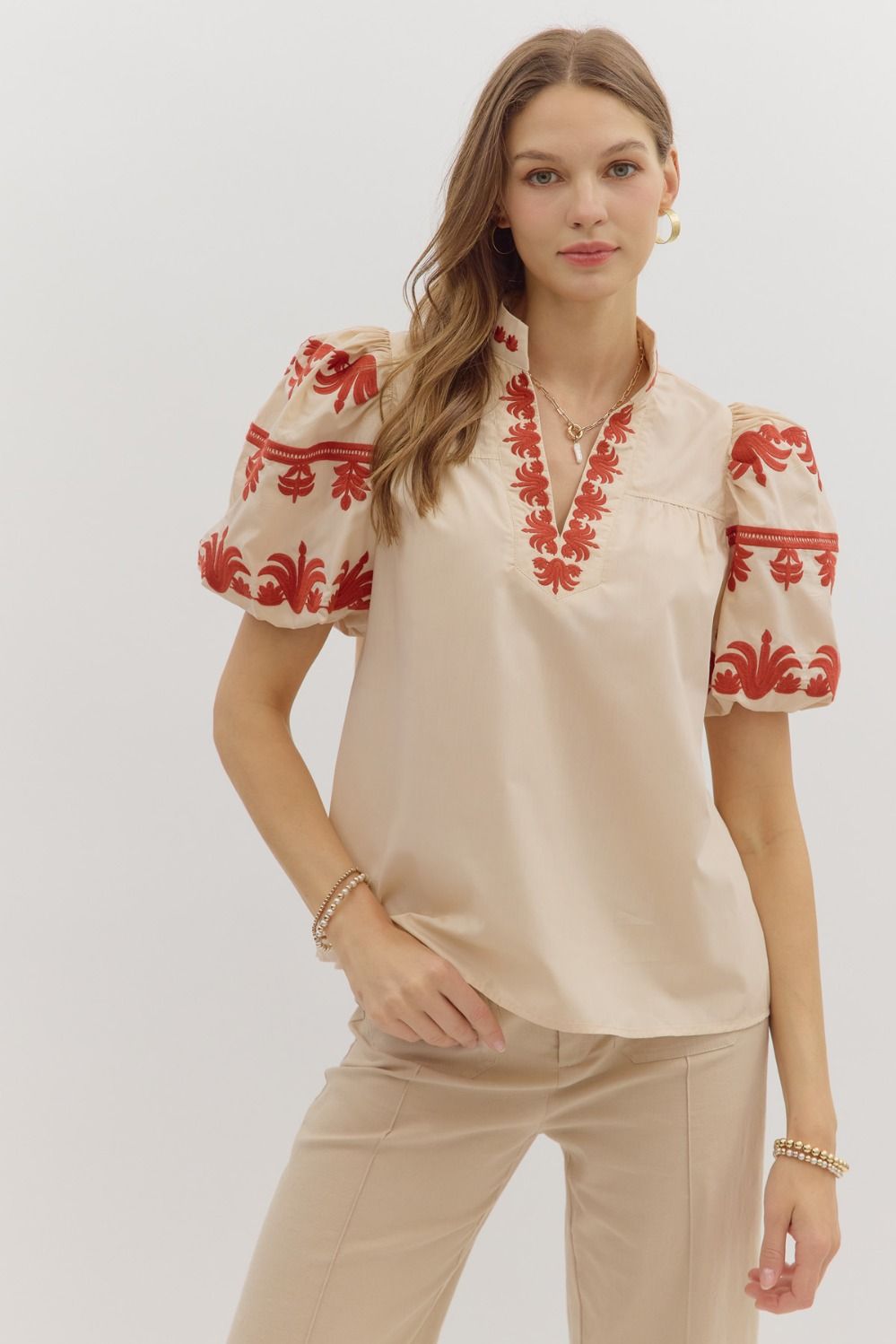 Woman wearing a beige blouse with red floral embroidery on a plain background