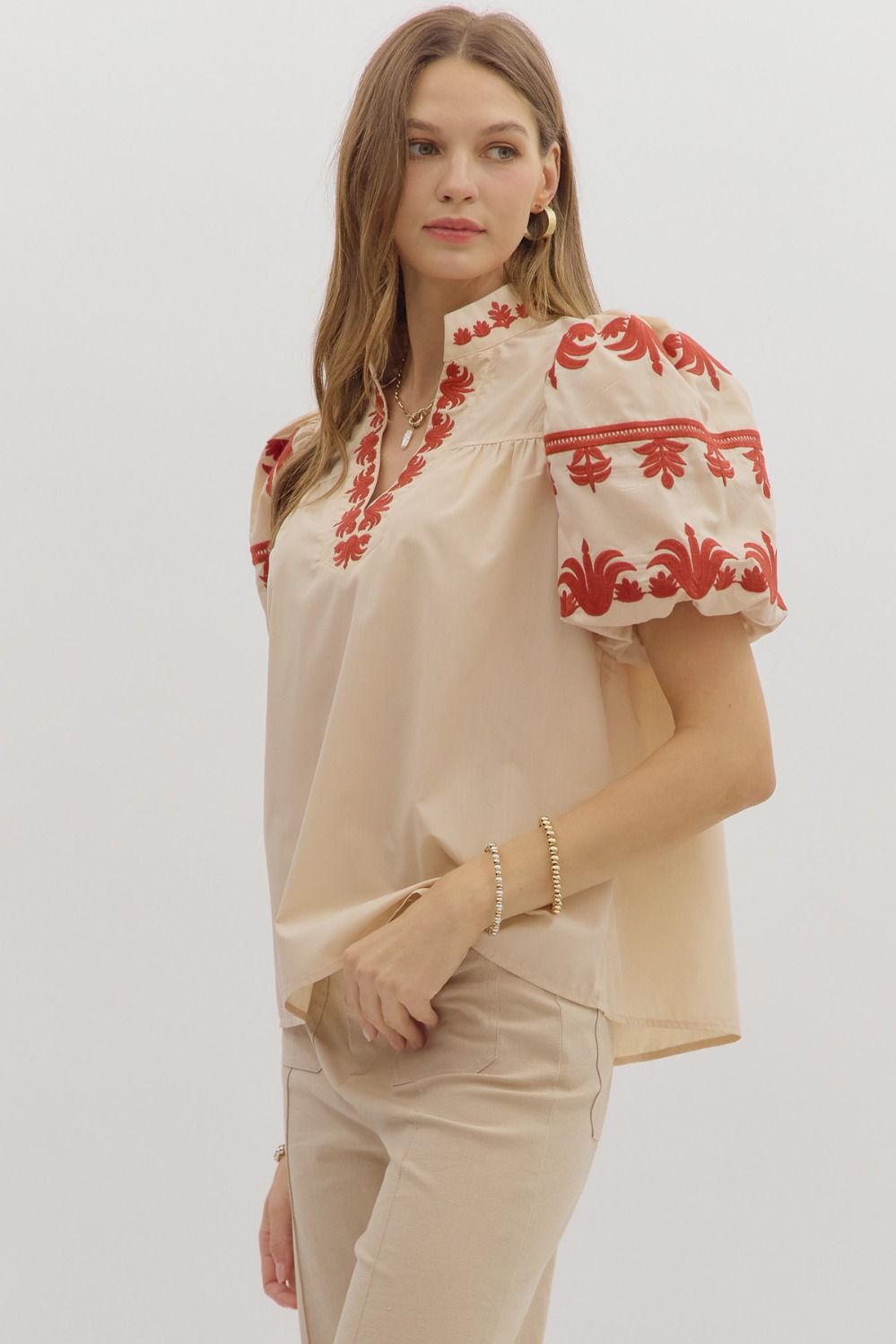Woman wearing a beige blouse with red embroidery on a white background