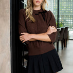 Woman wearing a brown sweater and black pleated skirt in an indoor setting
