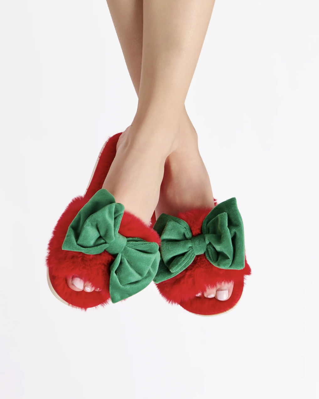 Red slippers with green bows worn by a person on a white background