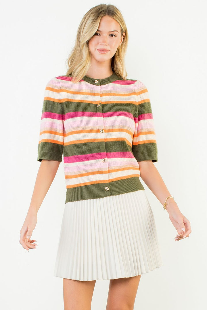 Woman wearing a colorful striped sweater and white pleated skirt on a white background