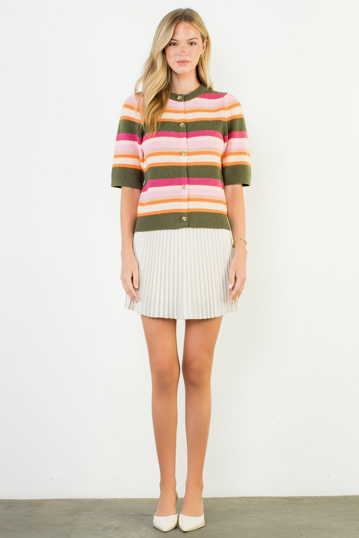 Woman wearing a colorful striped sweater and white skirt on a plain background
