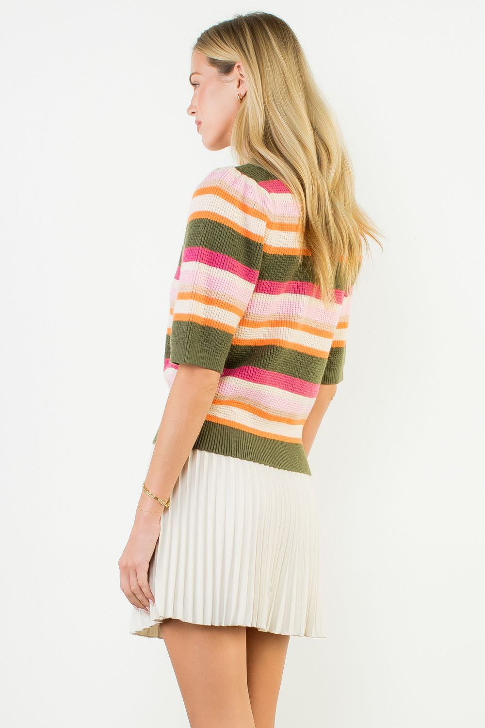 Woman wearing a colorful striped sweater and white pleated skirt on a white background