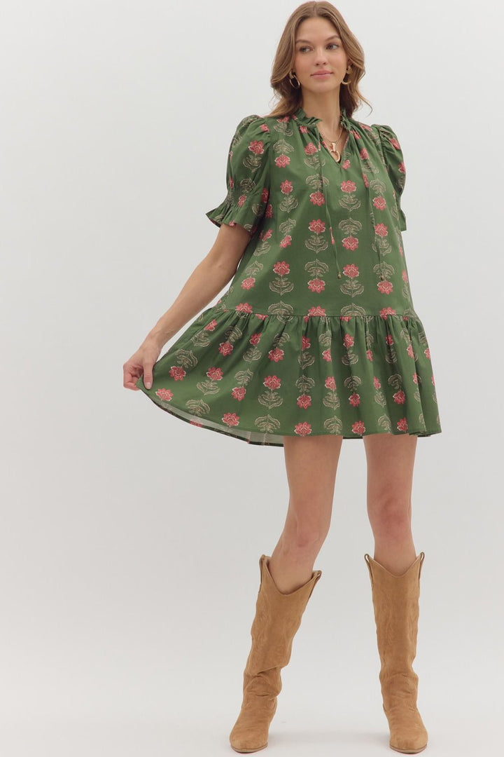 Woman wearing a green floral dress with brown boots on a white background