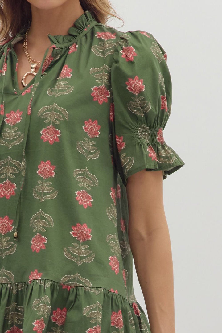 Green dress with pink floral pattern worn by a person on a white background