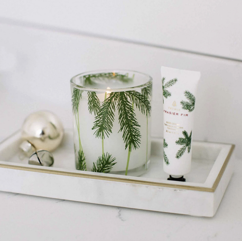 Candle with green foliage design and a matching tube of hand cream on a marble tray.