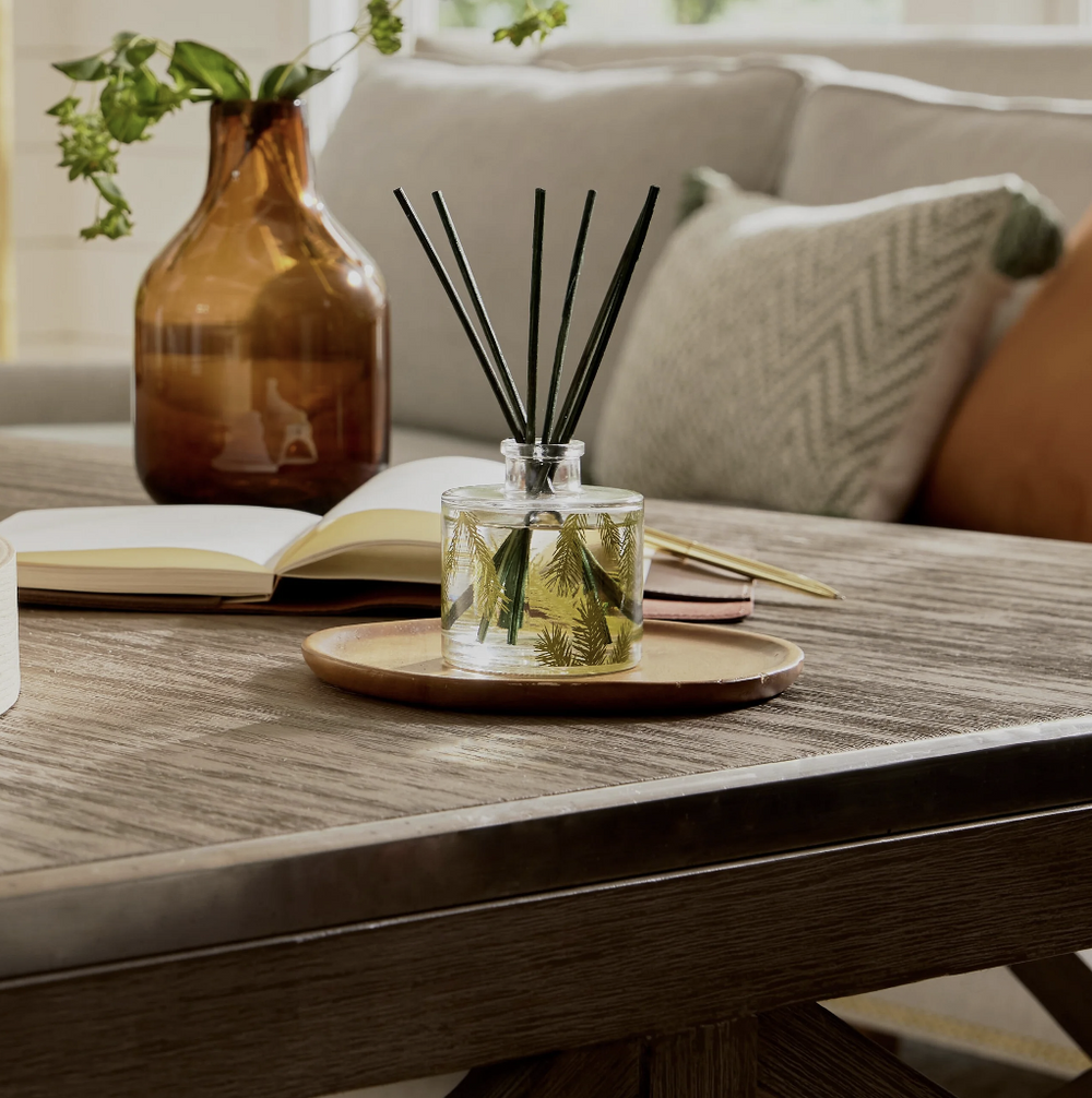 A diffuser with reeds on a wooden table in a cozy living room setting.