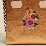Point of Origin Consuela Bronzed Classic Tote with metallic finish, floral embroidery, and woven striped handles.