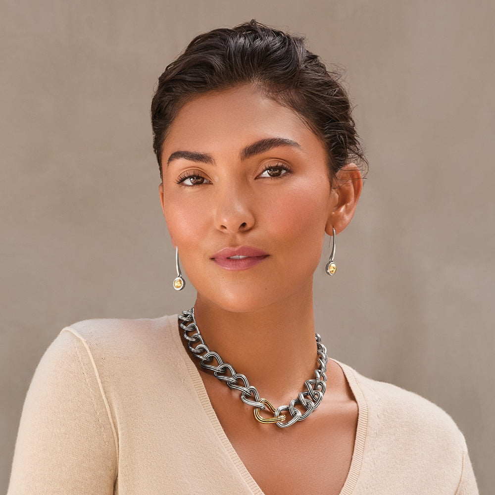 Woman wearing a silver chain necklace and earrings against a beige background