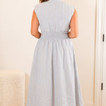 Woman in a light blue dress standing in a room with a mirror and furniture.