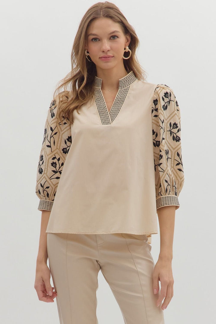 Woman wearing a beige blouse with floral embroidery on sleeves against a white background
