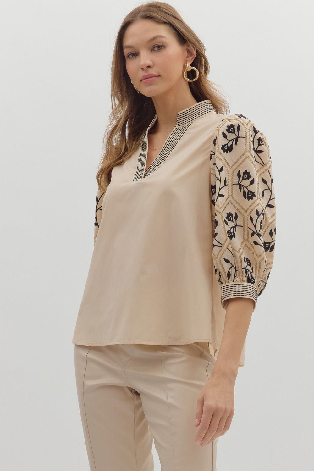 Woman wearing a beige blouse with black floral patterns on sleeves against a white background