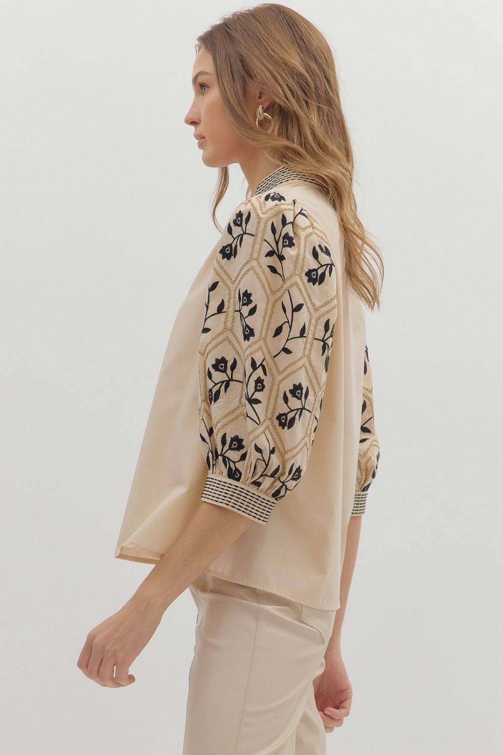 Woman wearing a beige patterned top with a plain background