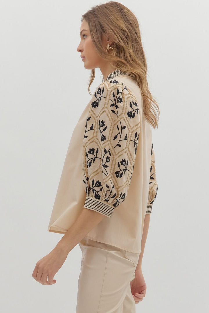 Woman wearing a beige patterned top with a plain background