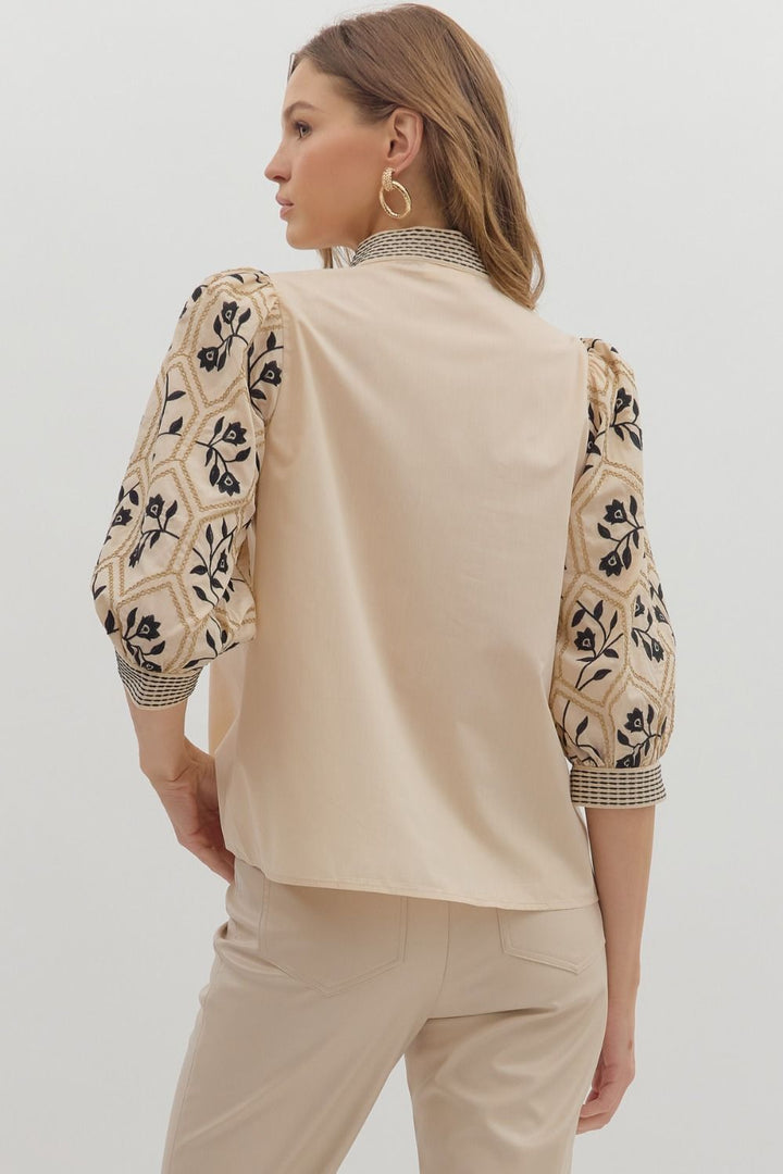 Woman wearing a beige top with floral sleeves on a plain background