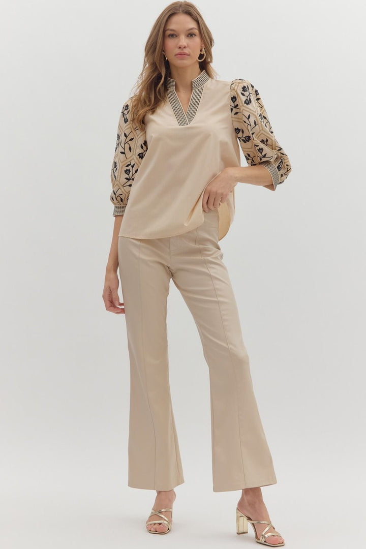 Woman wearing a beige top with floral sleeves and matching pants on a white background