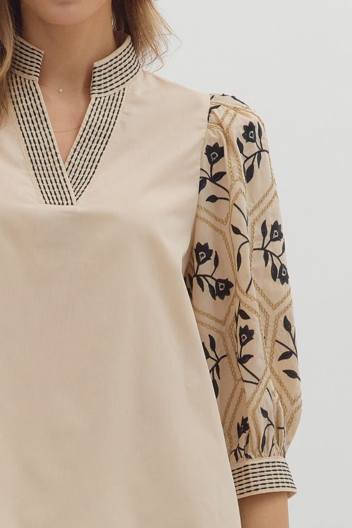 Beige long-sleeve top with black floral patterns on a plain background