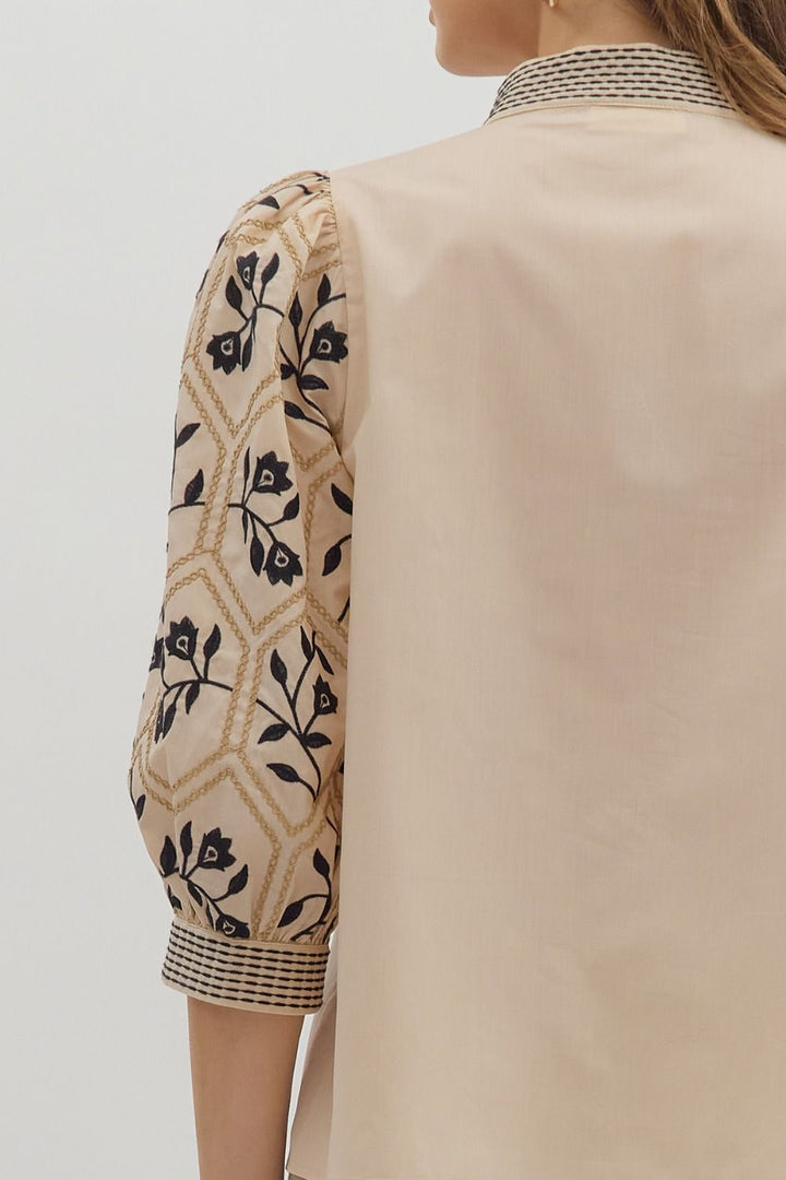 Beige outfit with floral embroidery on sleeves against a neutral background