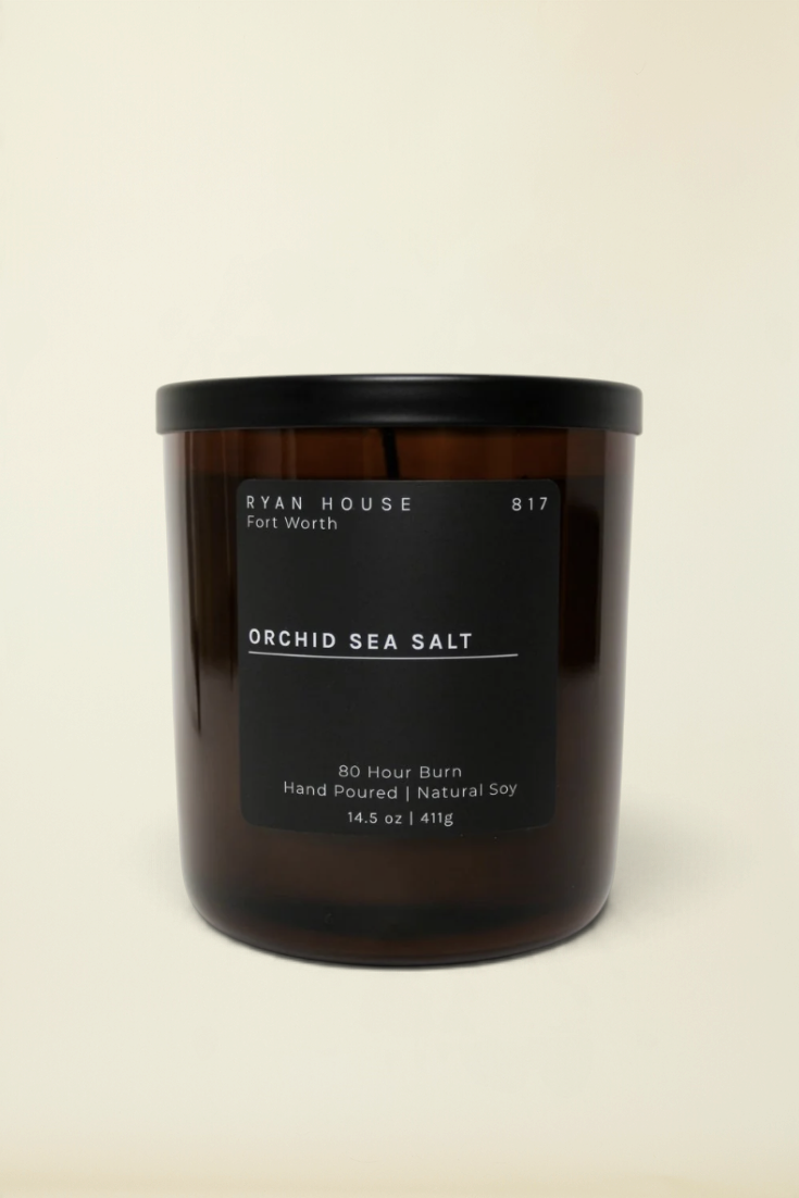 Point of Origin Ryan House Orchid Sea Salt soy candle in an amber glass jar with a black lid on a white background.