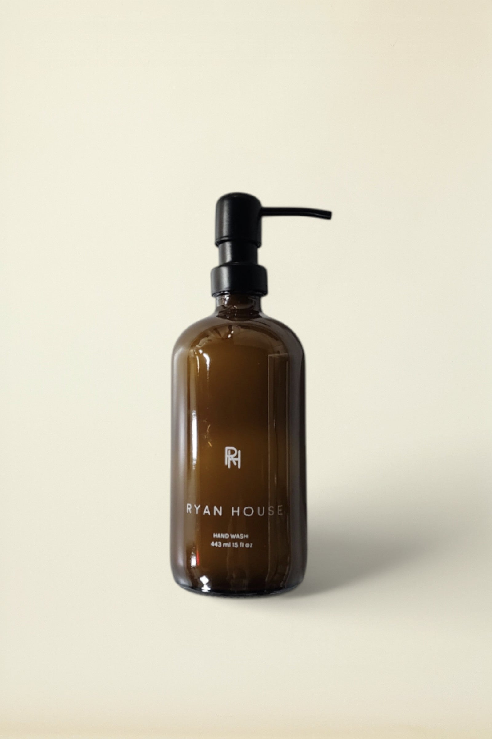 Ryan House hand wash in an amber glass bottle with a black pump dispenser, set against a solid cream background.