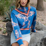 Woman wearing a blue patterned sweater sitting on a log outdoors