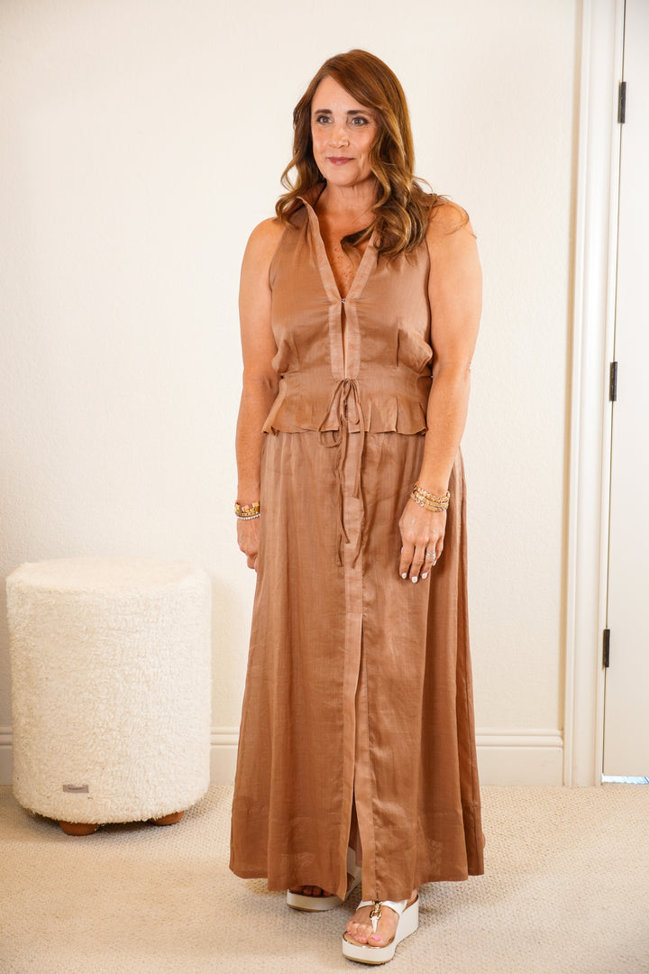 Woman wearing a brown dress standing in a room with a white wall and a textured white ottoman.