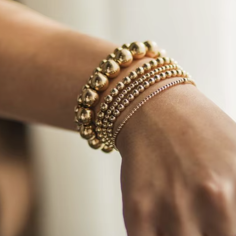 Hand wearing multiple gold bracelets on a blurred background