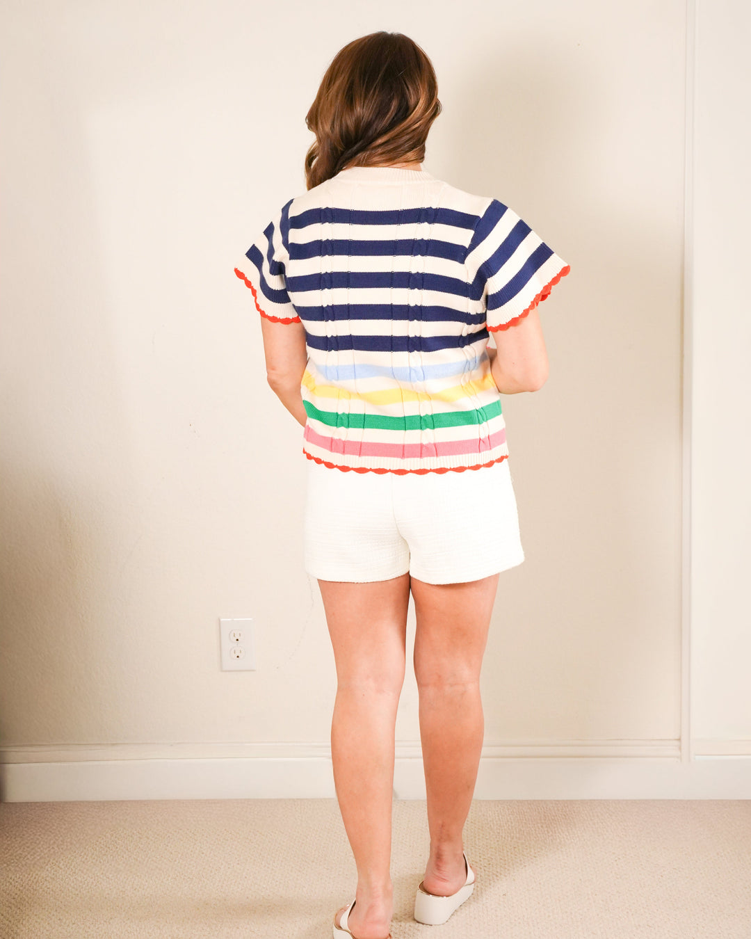 The Carter: Woman in a navy and white nautical striped short sleeve sweater with a rainbow bottom and orange scalloped hem.