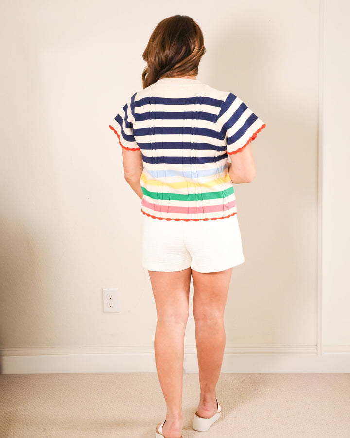 The Carter: Woman in a navy and white nautical striped short sleeve sweater with a rainbow bottom and orange scalloped hem.