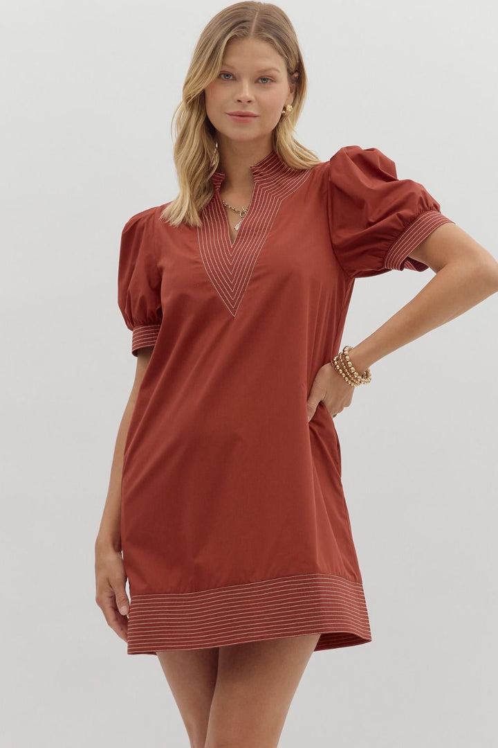 Woman wearing a rust-colored dress with puff sleeves on a plain background