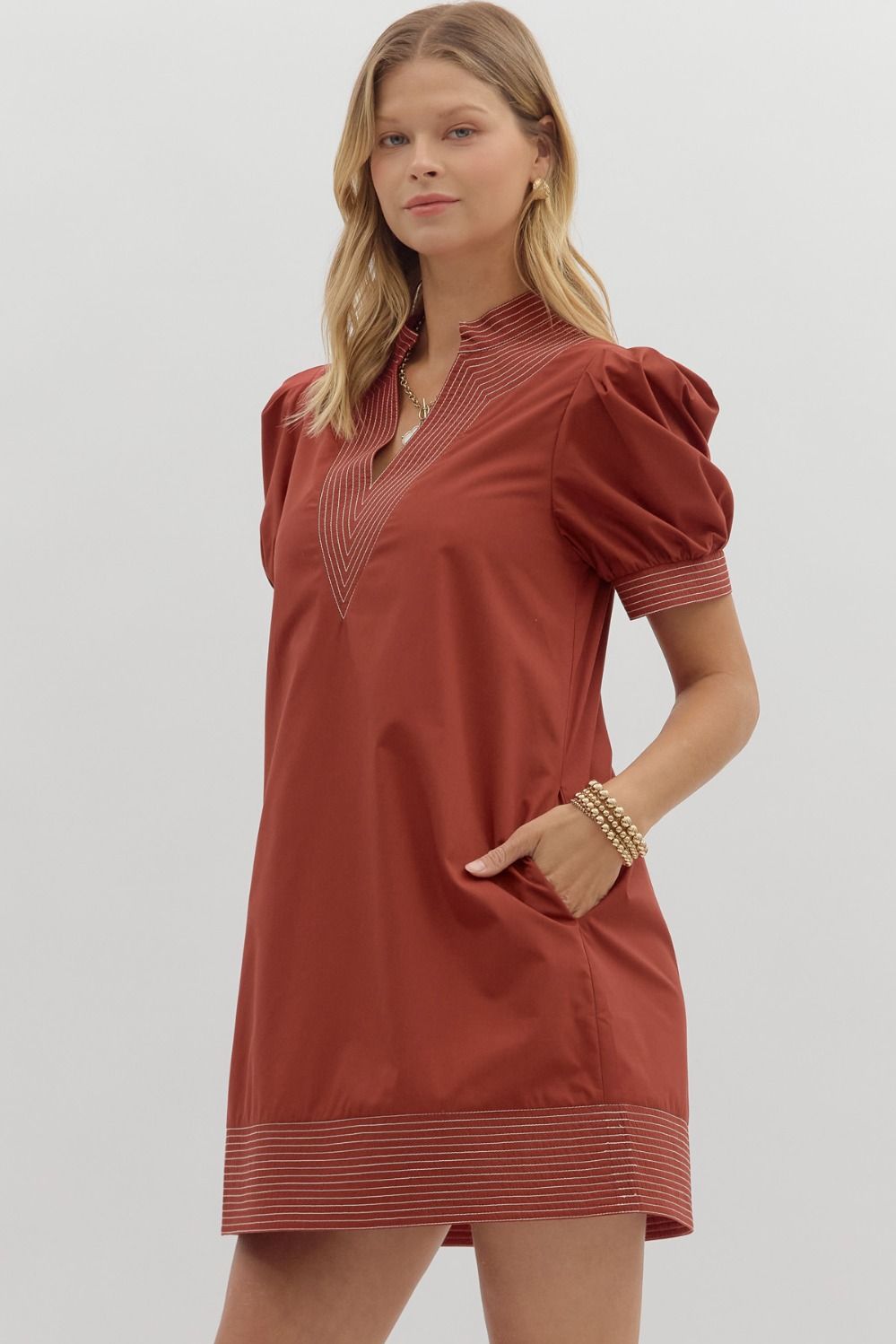 Woman wearing a rust-colored dress with puff sleeves on a light gray background