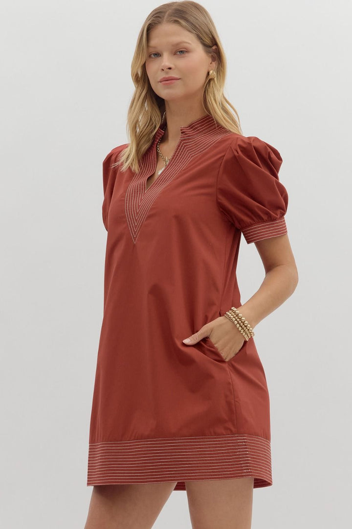 Woman wearing a rust-colored dress with puff sleeves on a light gray background