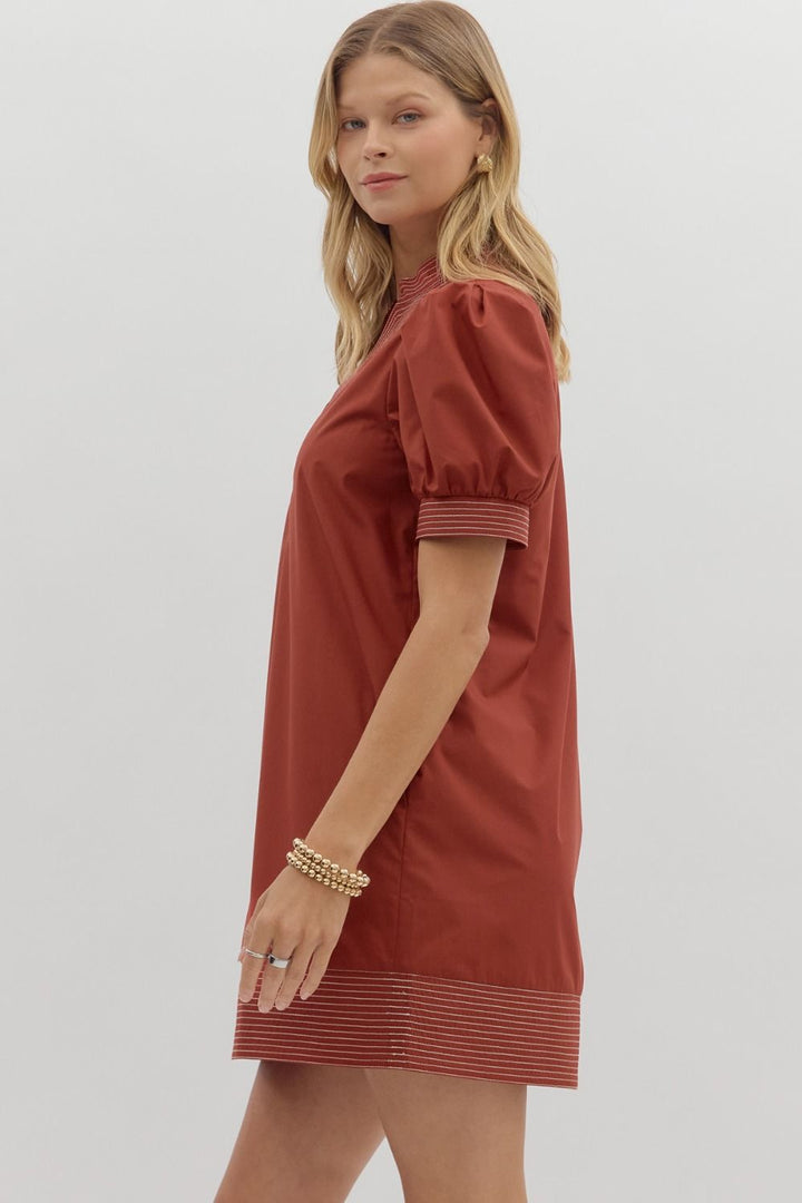 Woman wearing a rust-colored dress with short sleeves on a light gray background