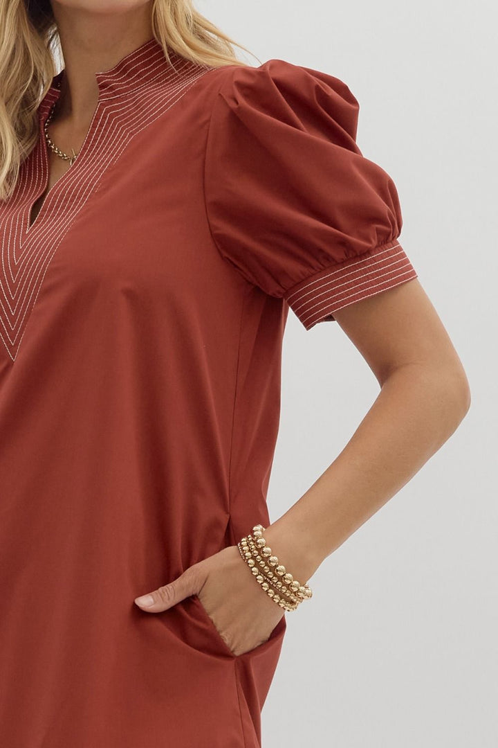 Woman wearing a rust-colored dress with puffed sleeves on a plain background