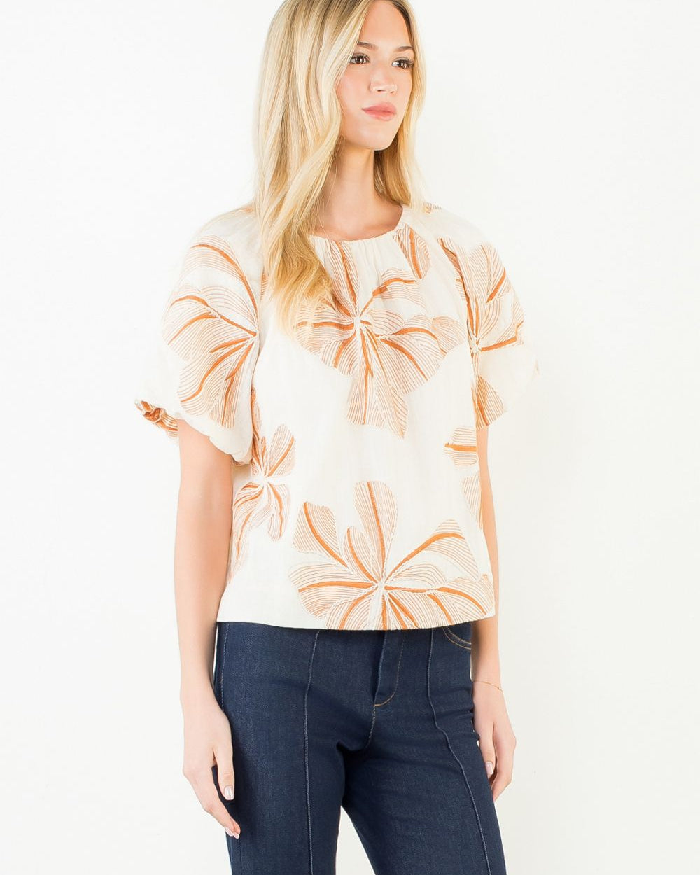 Woman wearing a beige floral blouse and dark jeans on a white background