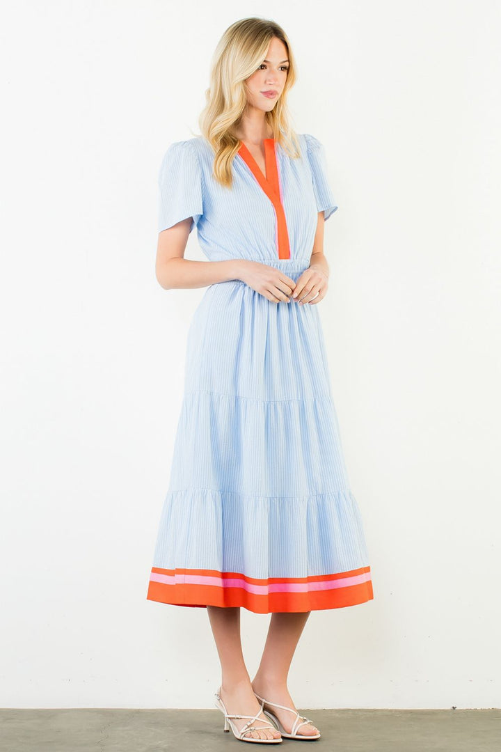 Woman wearing a light blue dress with orange accents against a white background