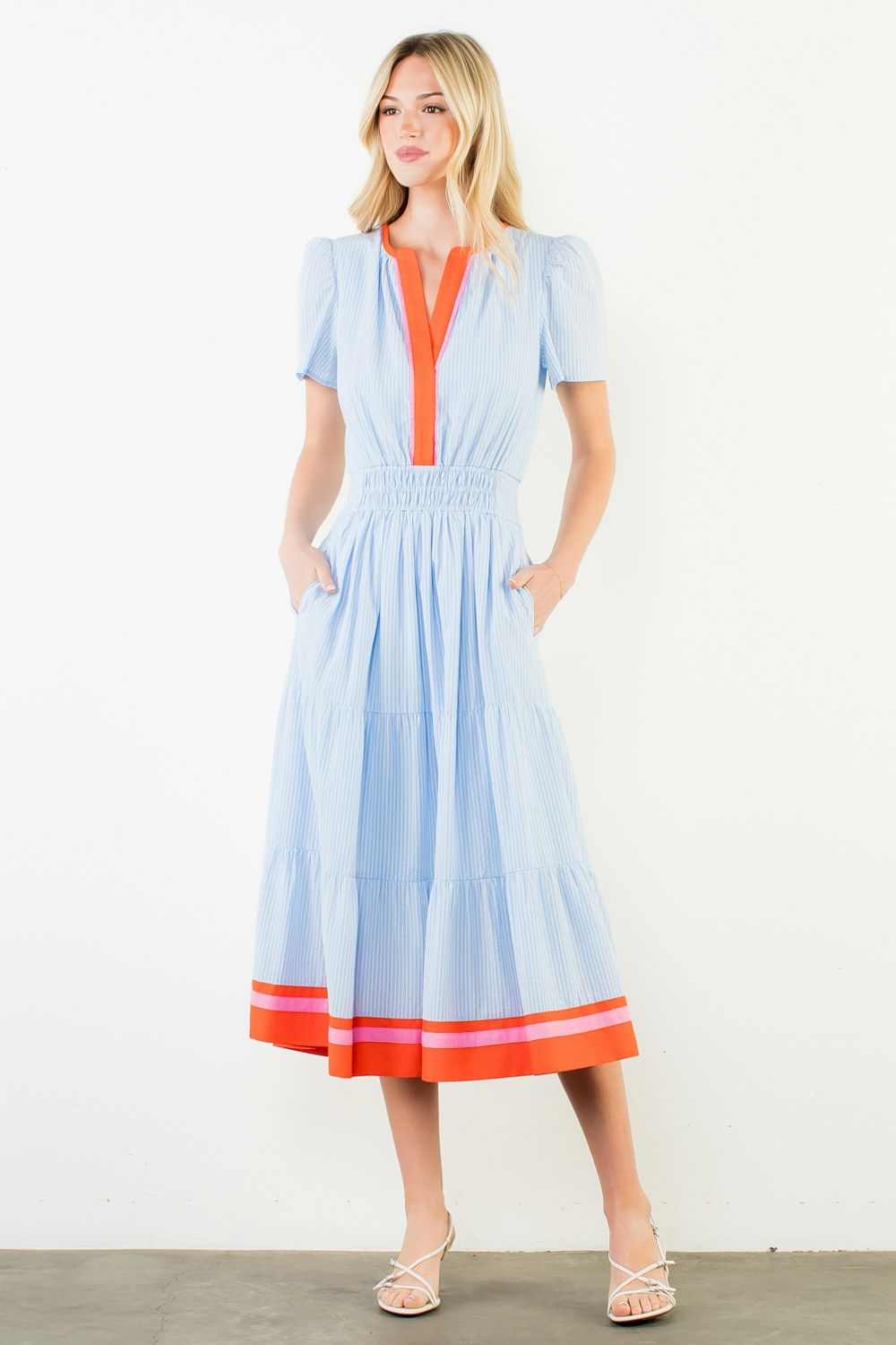 Woman wearing a light blue dress with orange accents on a white background